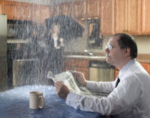 man sitting at kitchen table with water leaking through ceiling